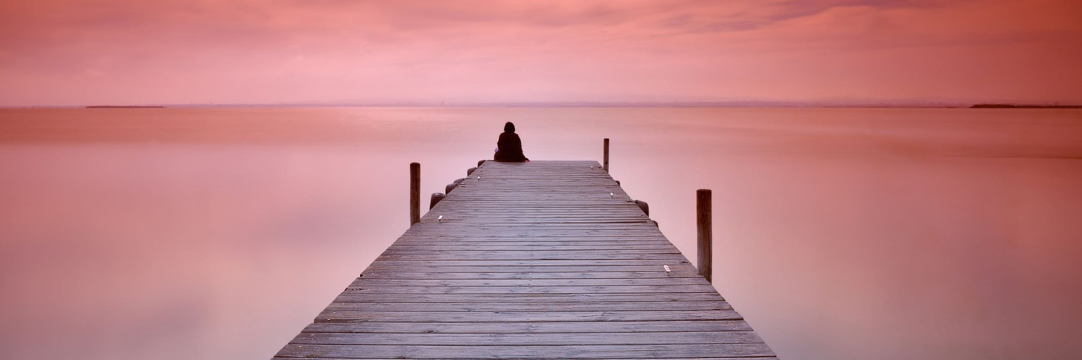 A person sitting alone at the end of a jetty on a calm evening. The scene depicts the Lonely Art of Art