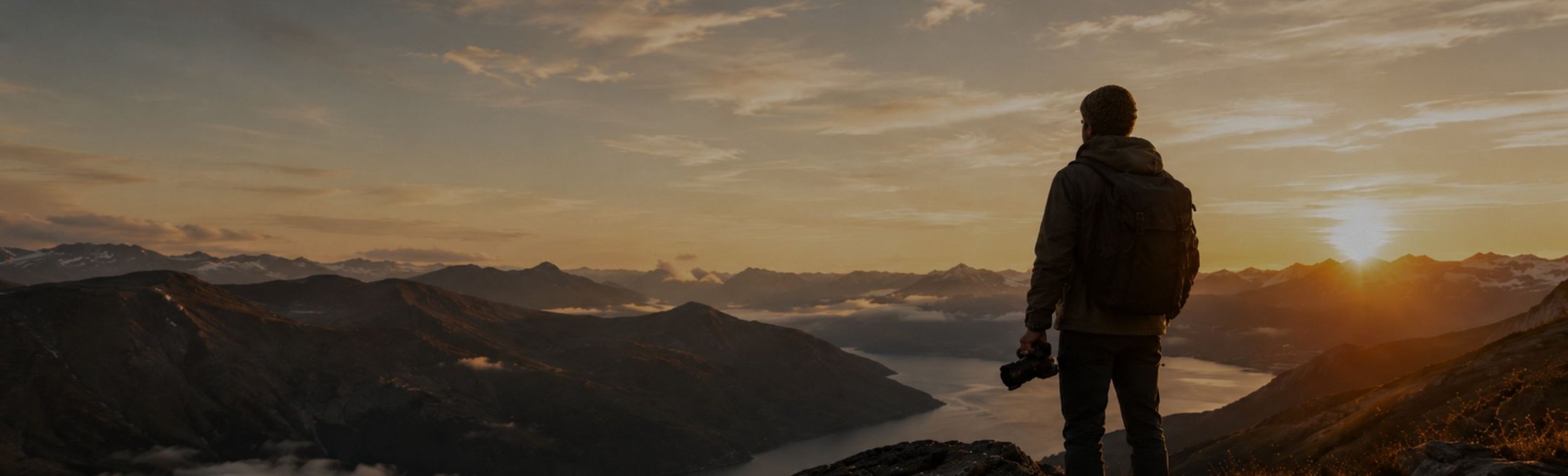 Photographer silhouetted on a ridge above a valley as the sun sets