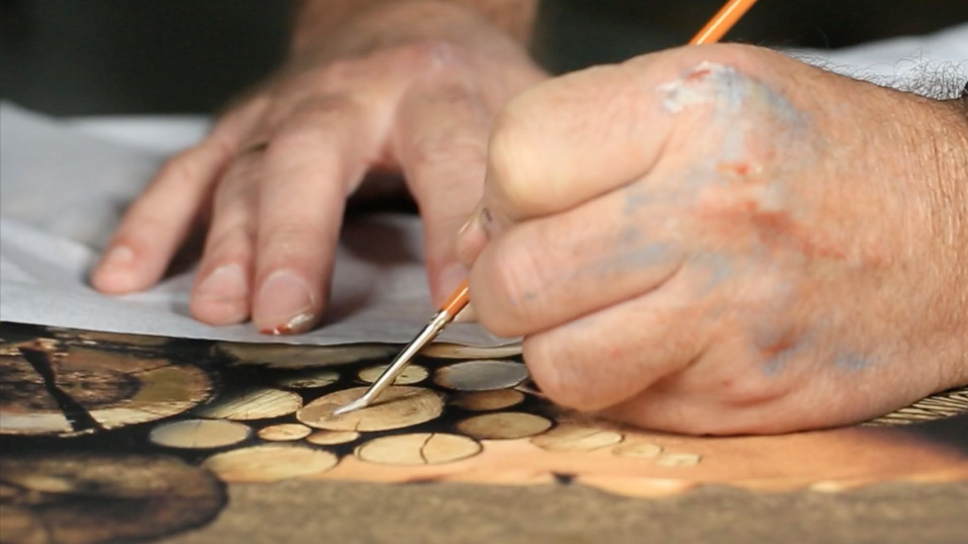 Artist painting intricate wood grain details on a canvas with a fine tip paintbrush.
