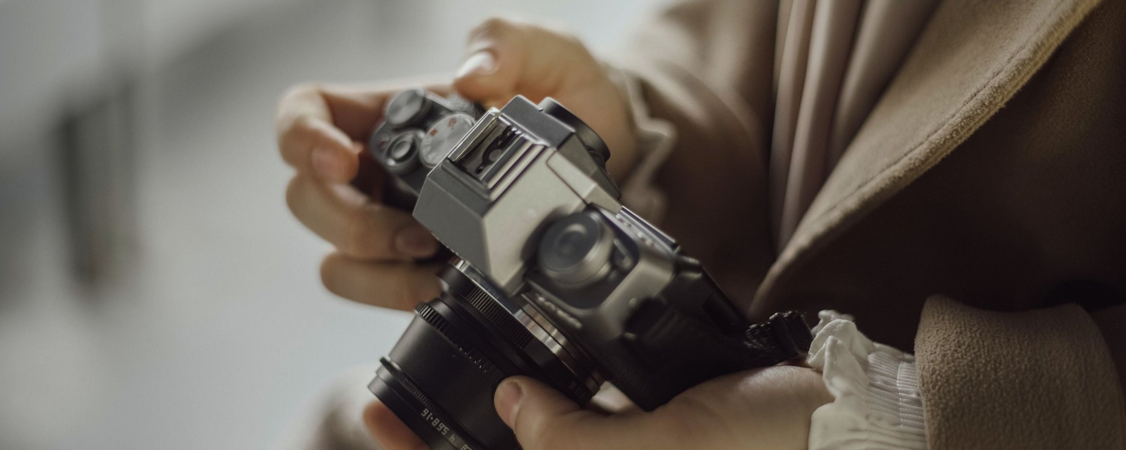 Close up of two hands holding a mirrorless camera, one thumb resting on the mode dial and the other fingers around the lens focus ring.