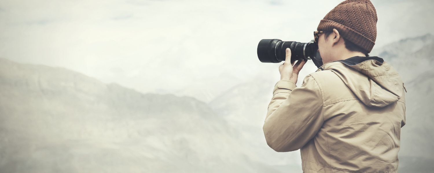 Photographer with a long lens looking out over misty mountains