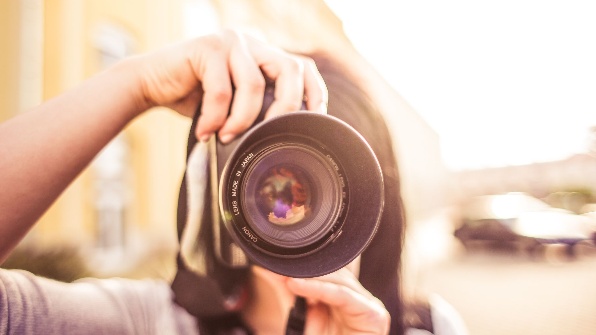 Photographer holding a camera up to her eye, lens facing the viewer