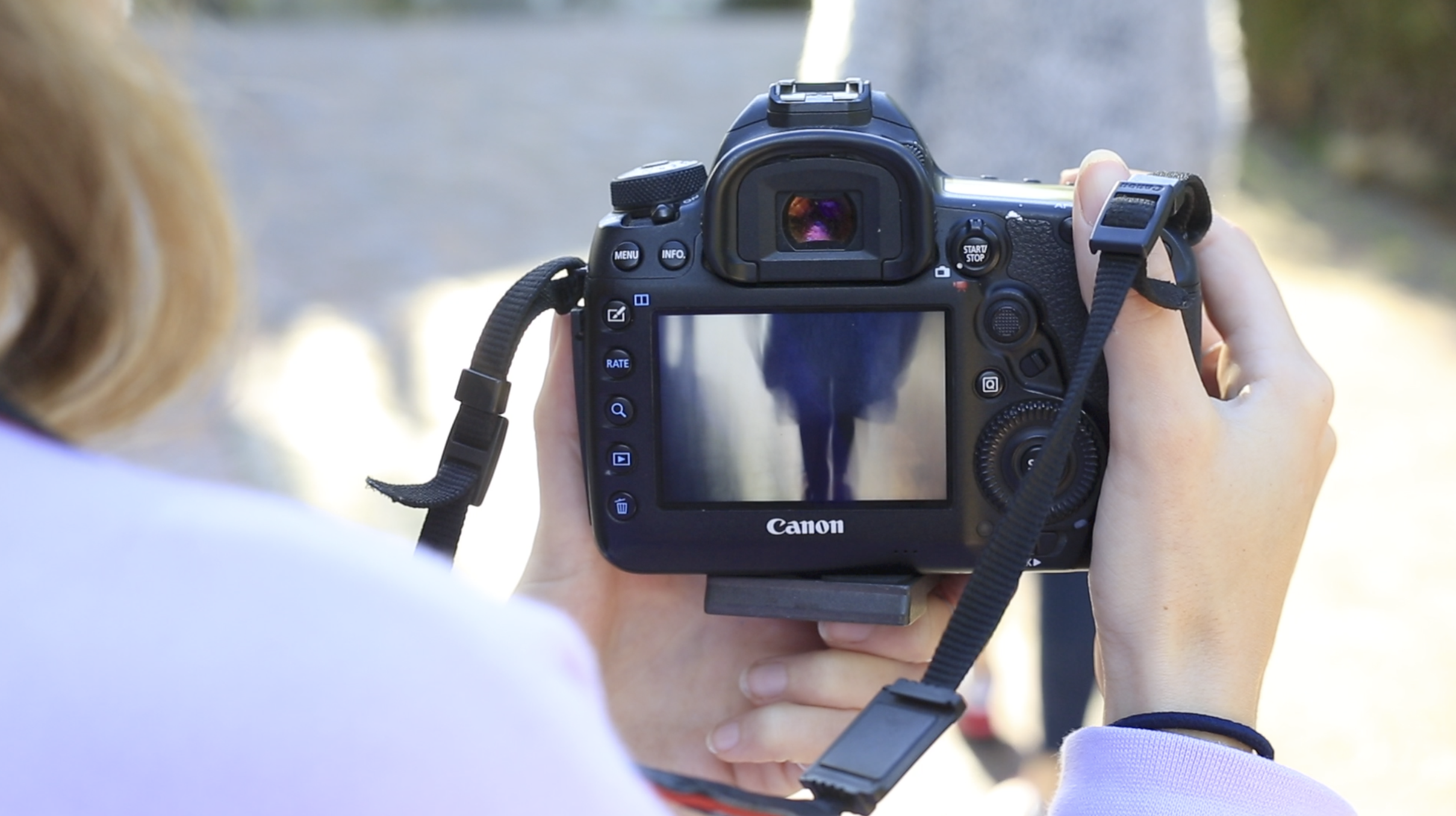 Photographer holding a Canon DSLR camera while reviewing photos on the LCD screen outdoors.