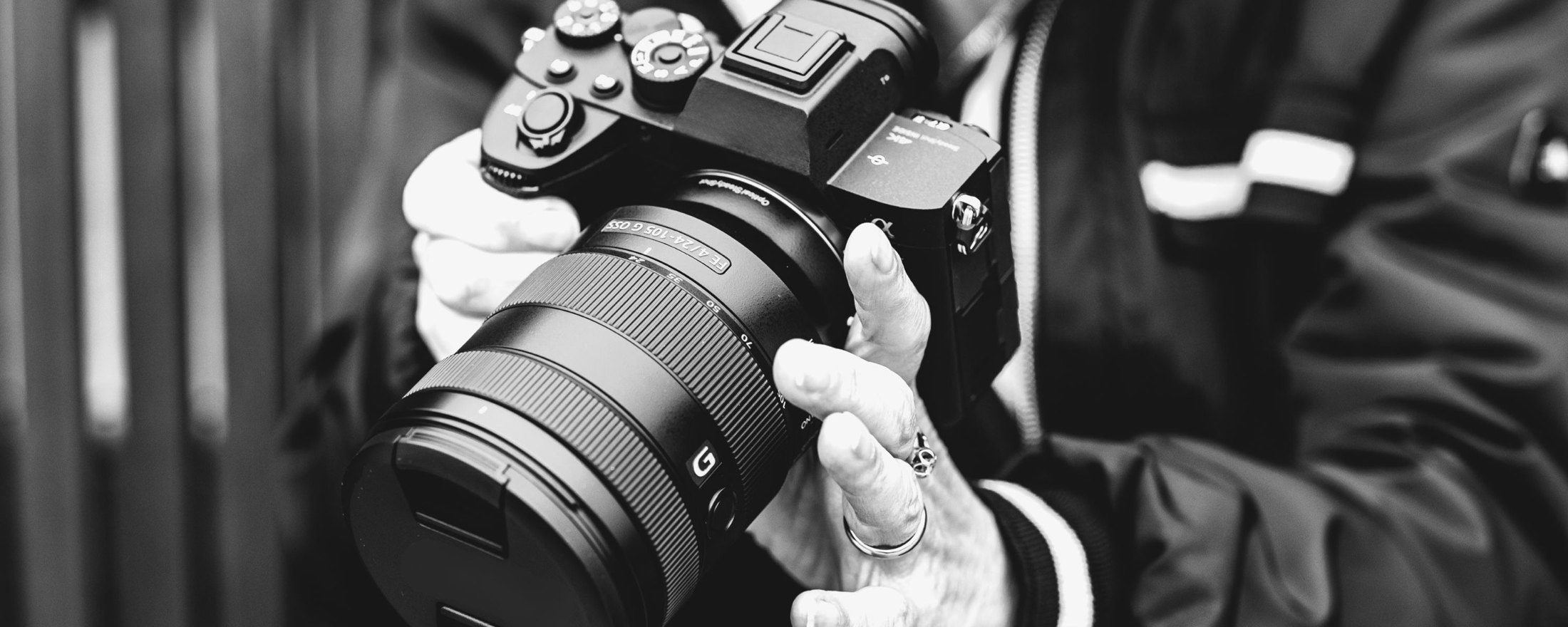 Hands holding a camera with a large lens, in black and white